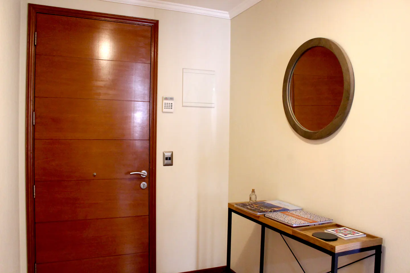 Entryway with a wooden door, security panel, and a console table with a round mirror above it.
