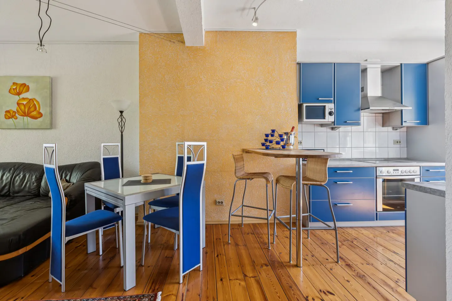 A modern apartment interior with a dining area and blue kitchen cabinets on a wooden floor.
