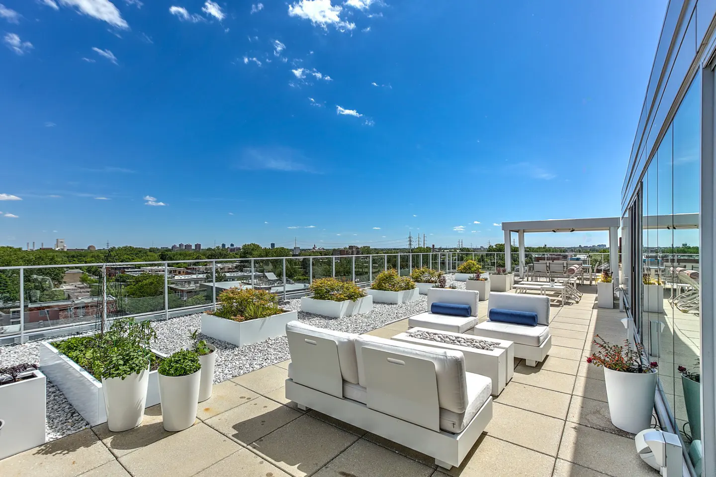 Rooftop patio with white furniture, planters, and gravel. City skyline and blue sky with clouds in the background.