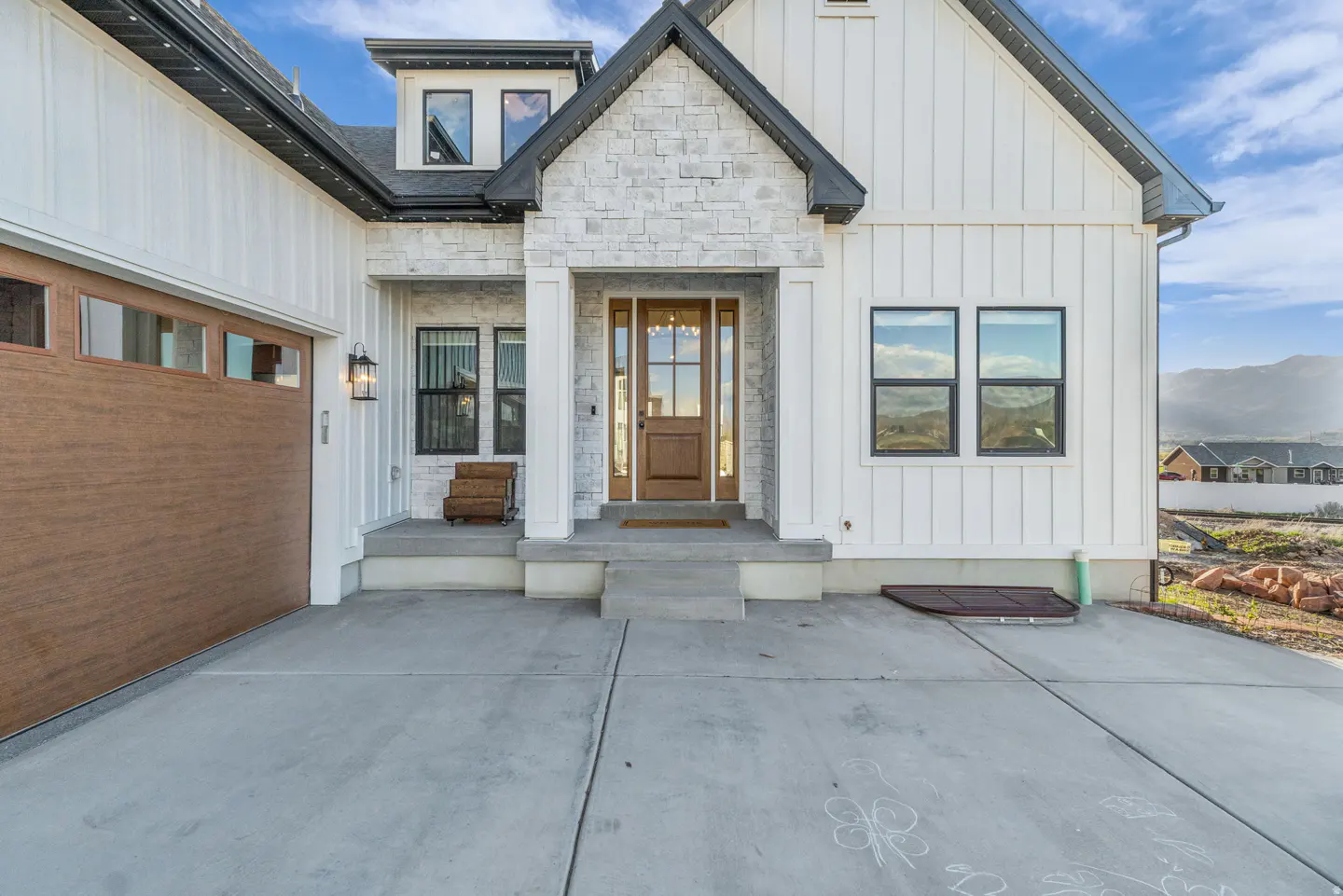 Front exterior of a modern farmhouse with white siding, stone accents, and a brown wood door and garage.