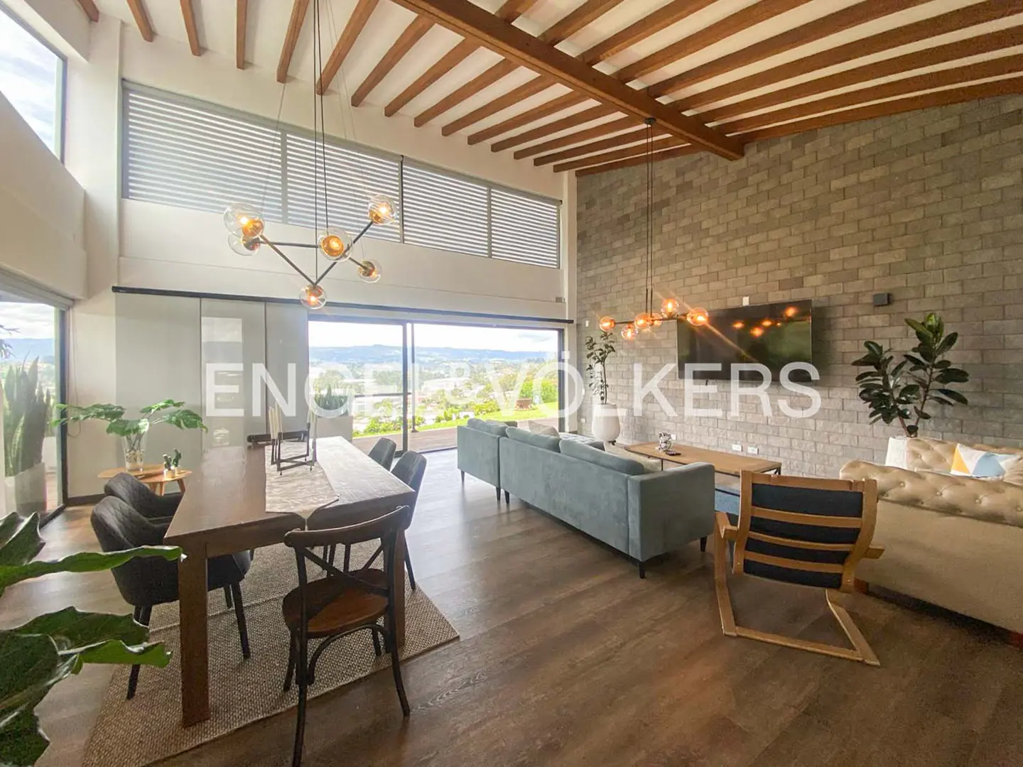 A bright living room with a dining table, blue sofa, brick wall, and large windows.