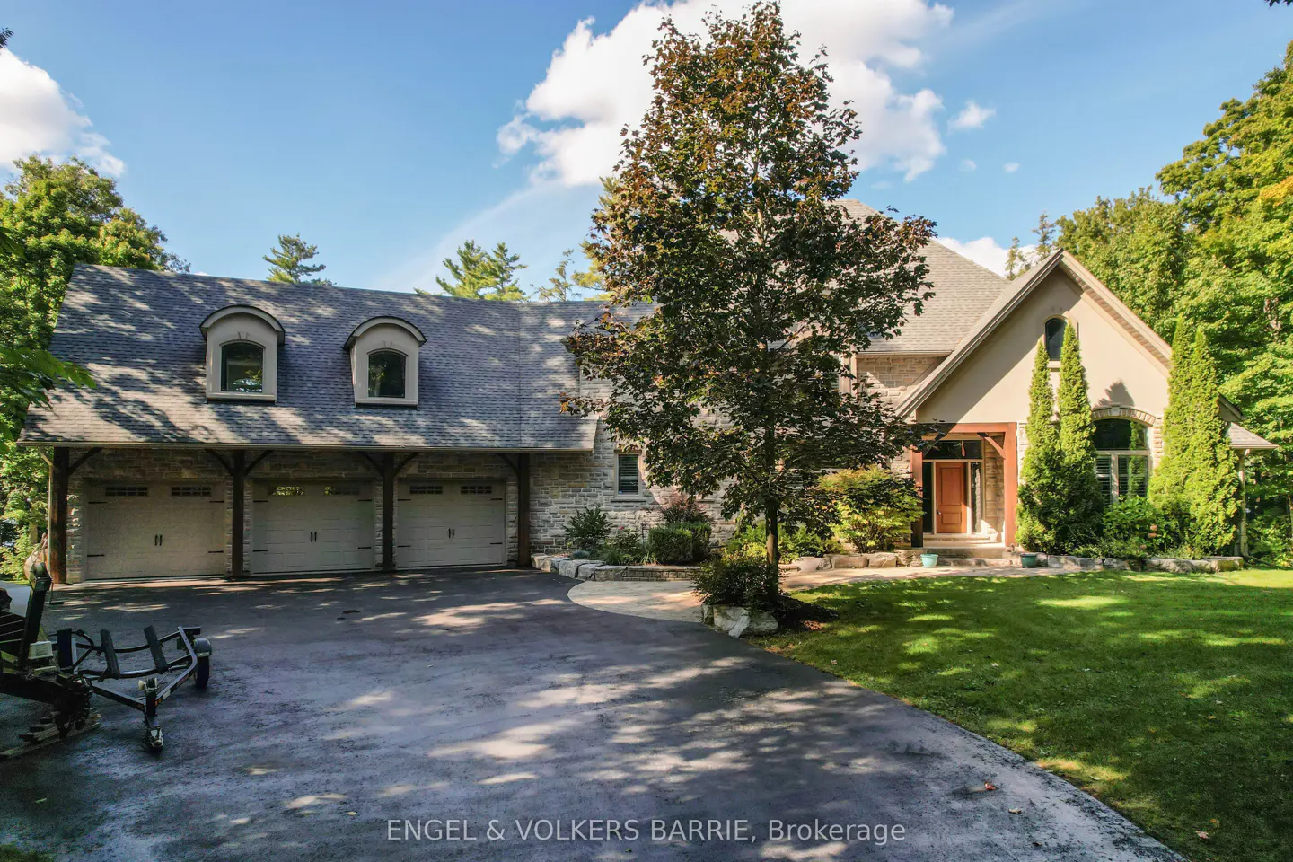 Exterior of a stone house with a three-car garage, a lawn, and a tree in front.