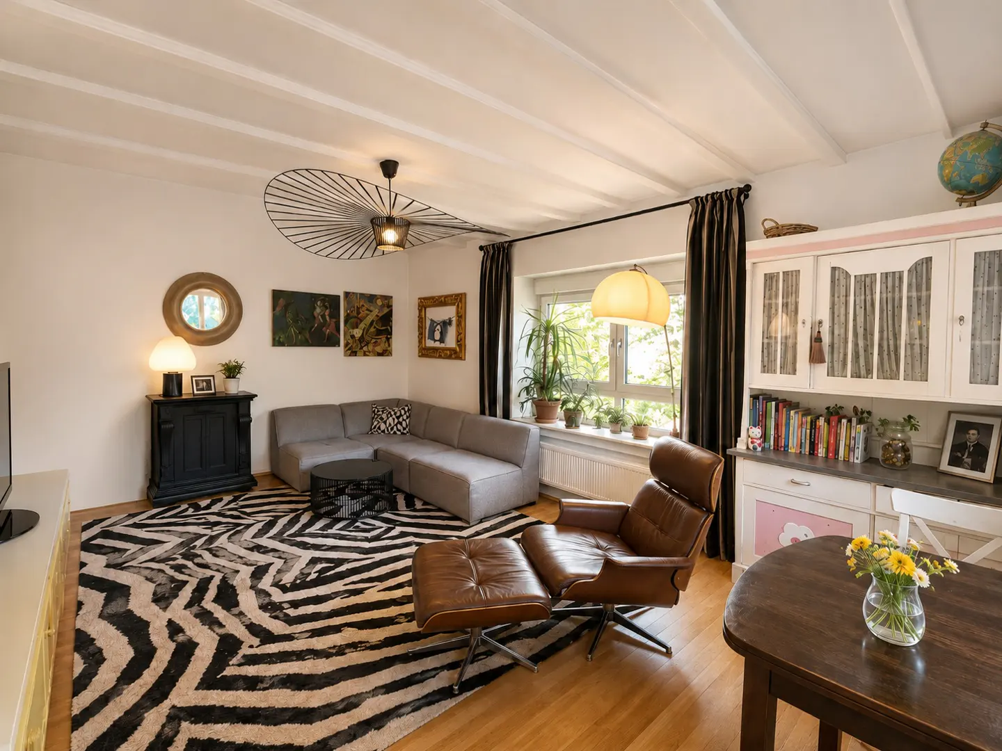 Living room with a gray sectional sofa, brown leather chair, and zebra-print rug. A unique light fixture hangs from the white ceiling.