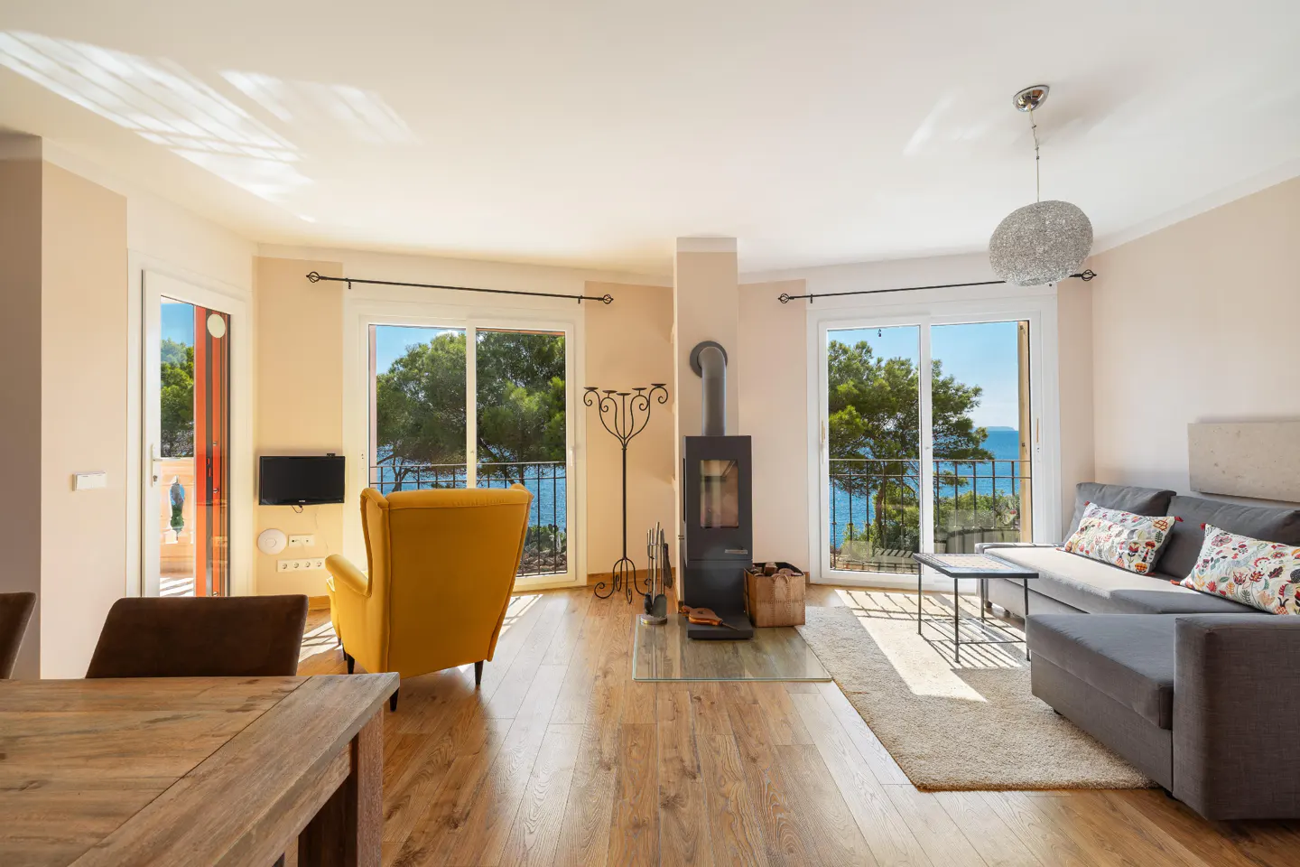 Bright living room with wood floors, a grey sofa, yellow chair, and a black fireplace. Balconies overlook the ocean.