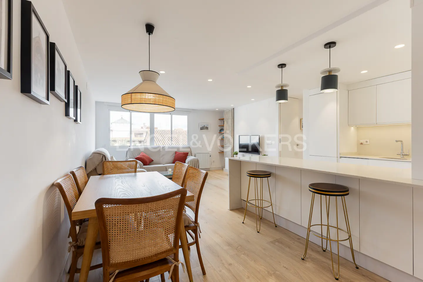Bright, open-concept living space with a dining table, kitchen island with stools, and a living room with a sofa.