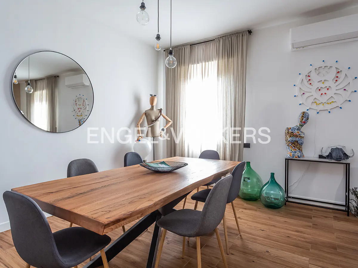 Bright dining room with a wood table, gray chairs, and wood floors. A round mirror and art decorate the white walls.