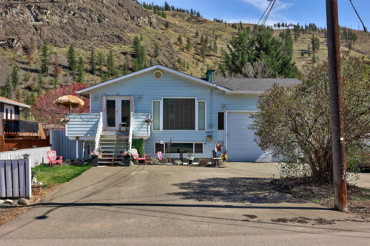 Light blue house with a front-facing garage and a deck with a straw umbrella, set against a mountain backdrop.