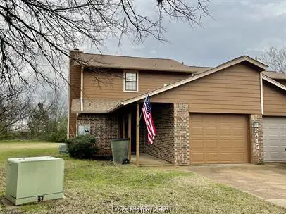 A two-story townhouse with brown siding, a brick facade, and an American flag hanging near the entrance.