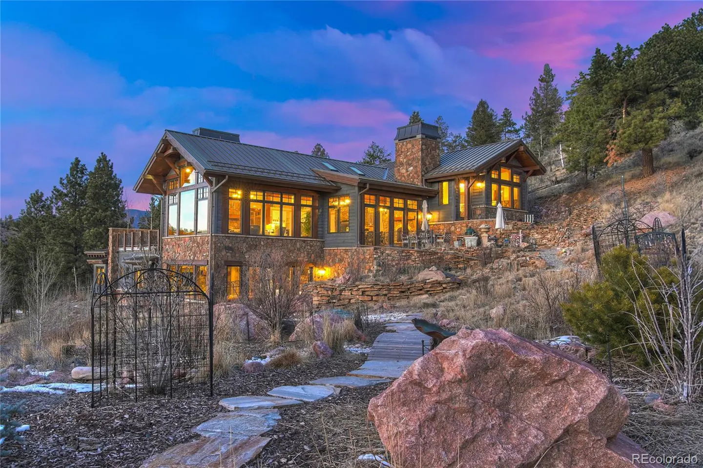 Exterior view of a stone and wood house on a hill at dusk with a stone path leading to the house.