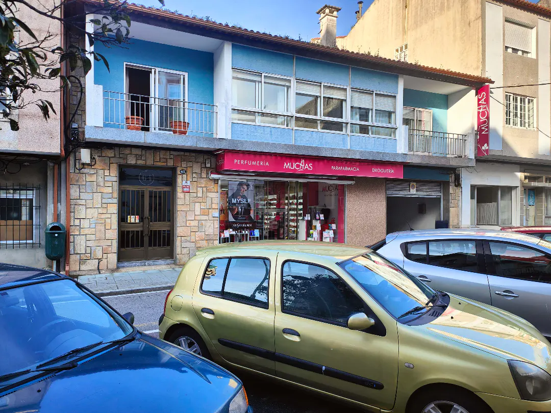 Two-story building with a blue facade above a storefront named "Muchas," with parked cars in front.