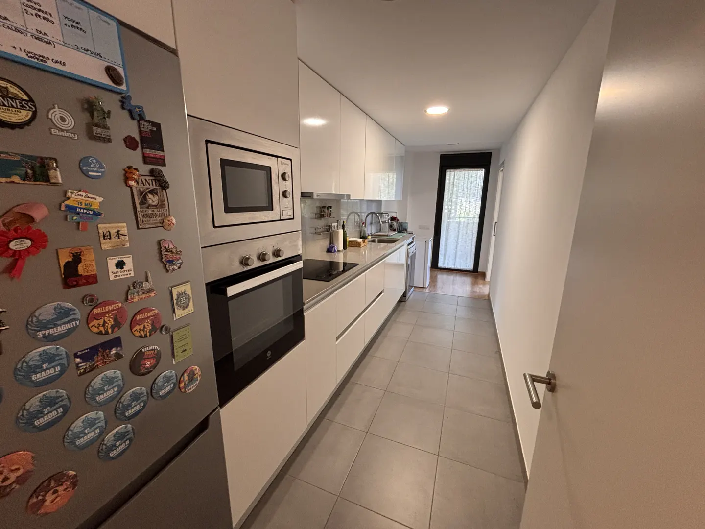 A modern kitchen with white cabinets, stainless steel appliances, and a refrigerator covered in magnets.