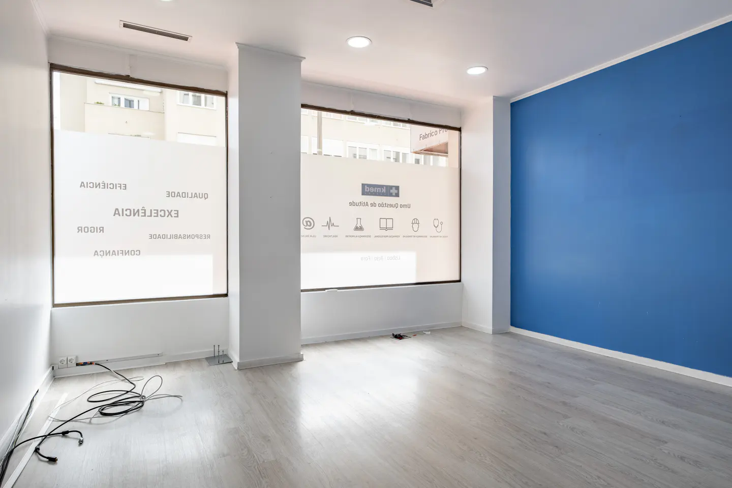 Empty office space with gray wood floors, white walls, and a blue accent wall. Large windows with frosted glass let in natural light.