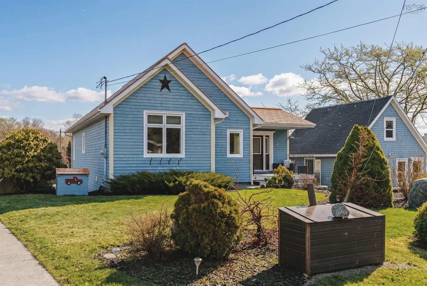 A light blue, one-story house with a star on the gable end, sits on a green lawn under a blue sky.