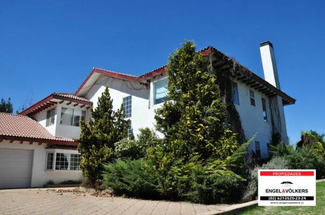 Exterior of a two-story white house with a red tile roof and a tall chimney, surrounded by green trees and bushes.