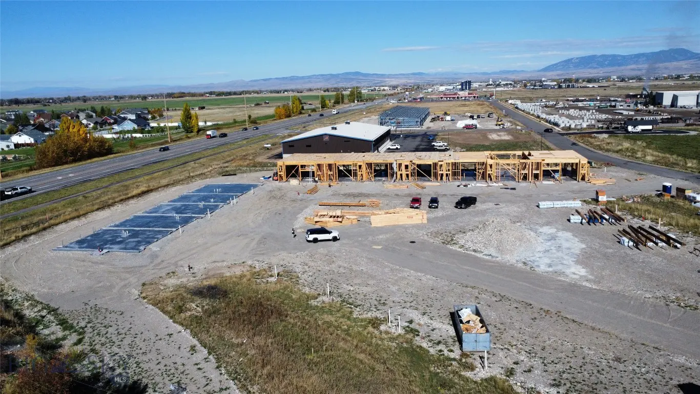 Aerial view of a new construction site with wood framing, concrete slabs, and lumber piles under a blue sky.