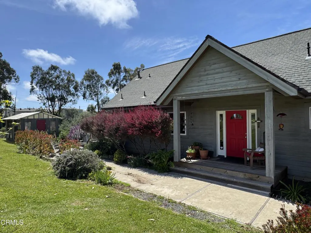 Exterior view of a gray house with a red front door, porch, and green lawn on a sunny day.