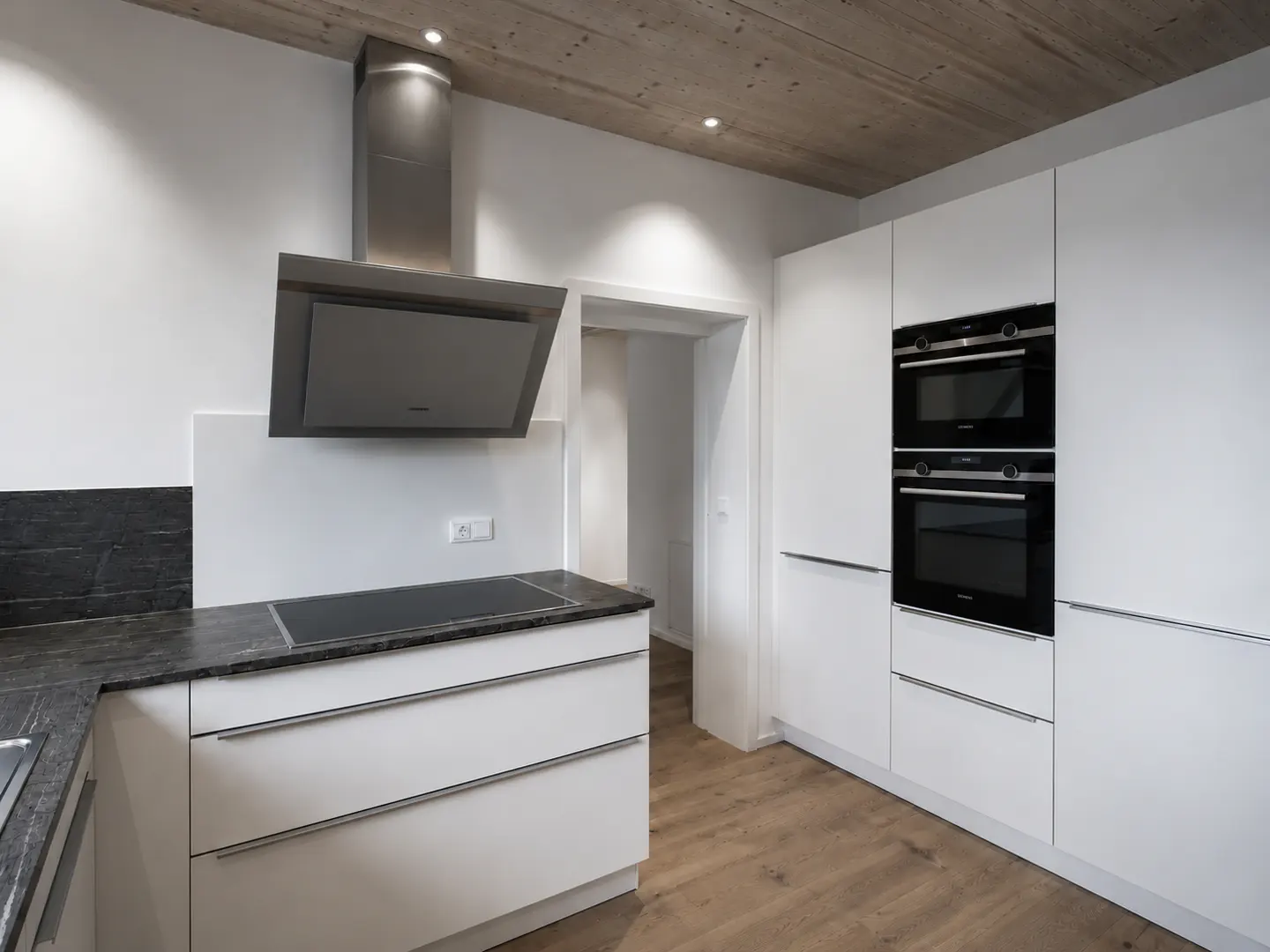 Modern kitchen with white cabinets, black countertops, and stainless steel appliances. Wood floor and concrete ceiling.
