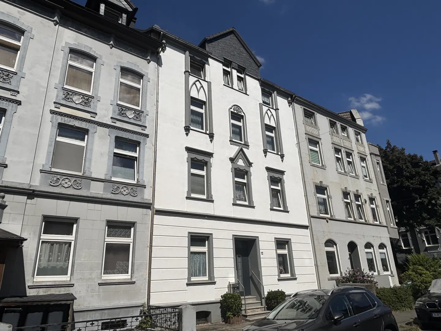 Three-story apartment buildings in gray and white, with decorative window frames, under a blue sky.