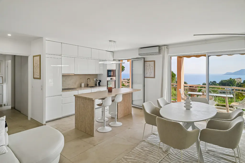 Modern open-plan kitchen and dining area with white cabinets, a wooden island, and a balcony overlooking the sea.