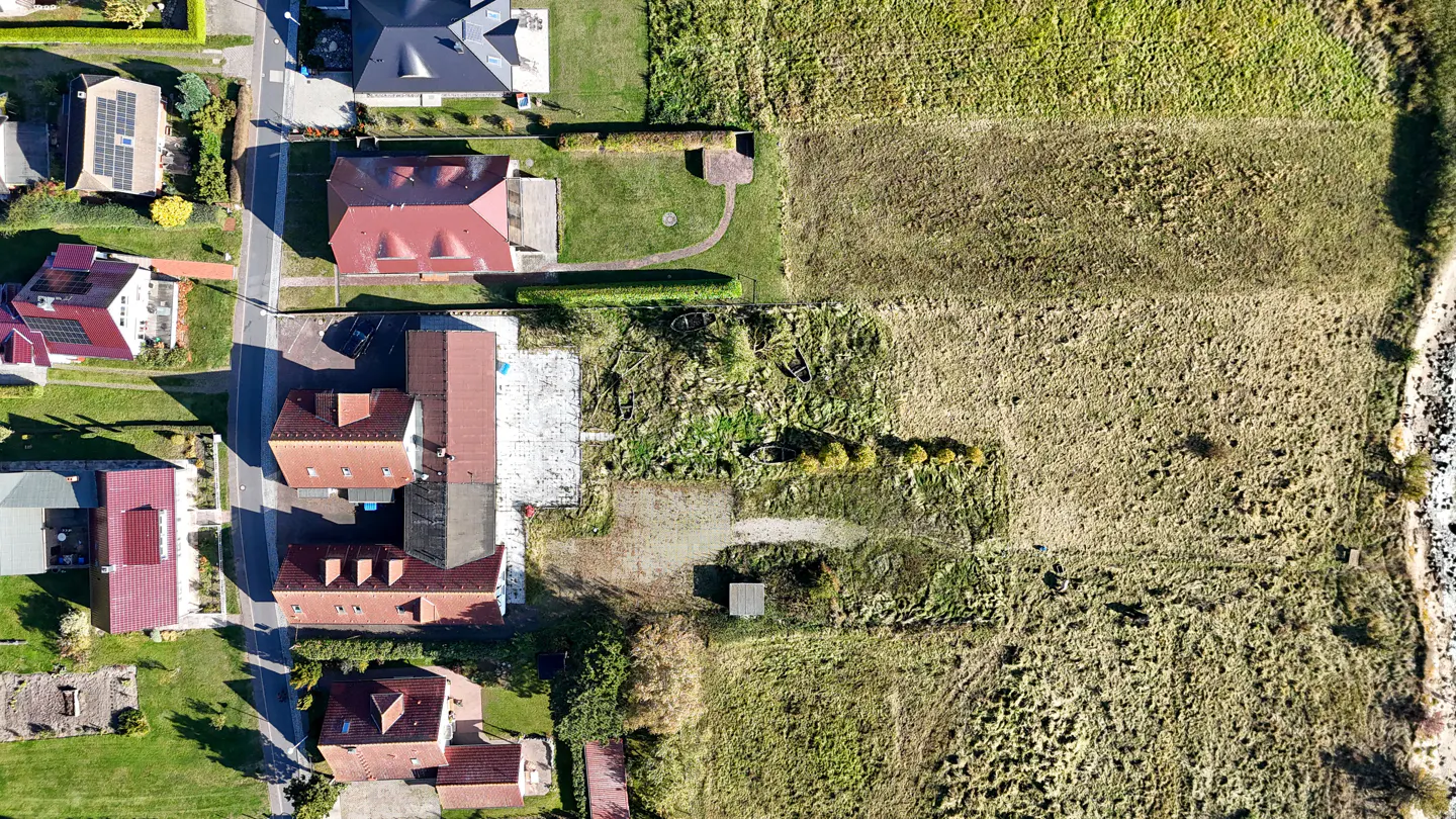 Aerial view of houses with red roofs and green lawns next to a field of dry grass.