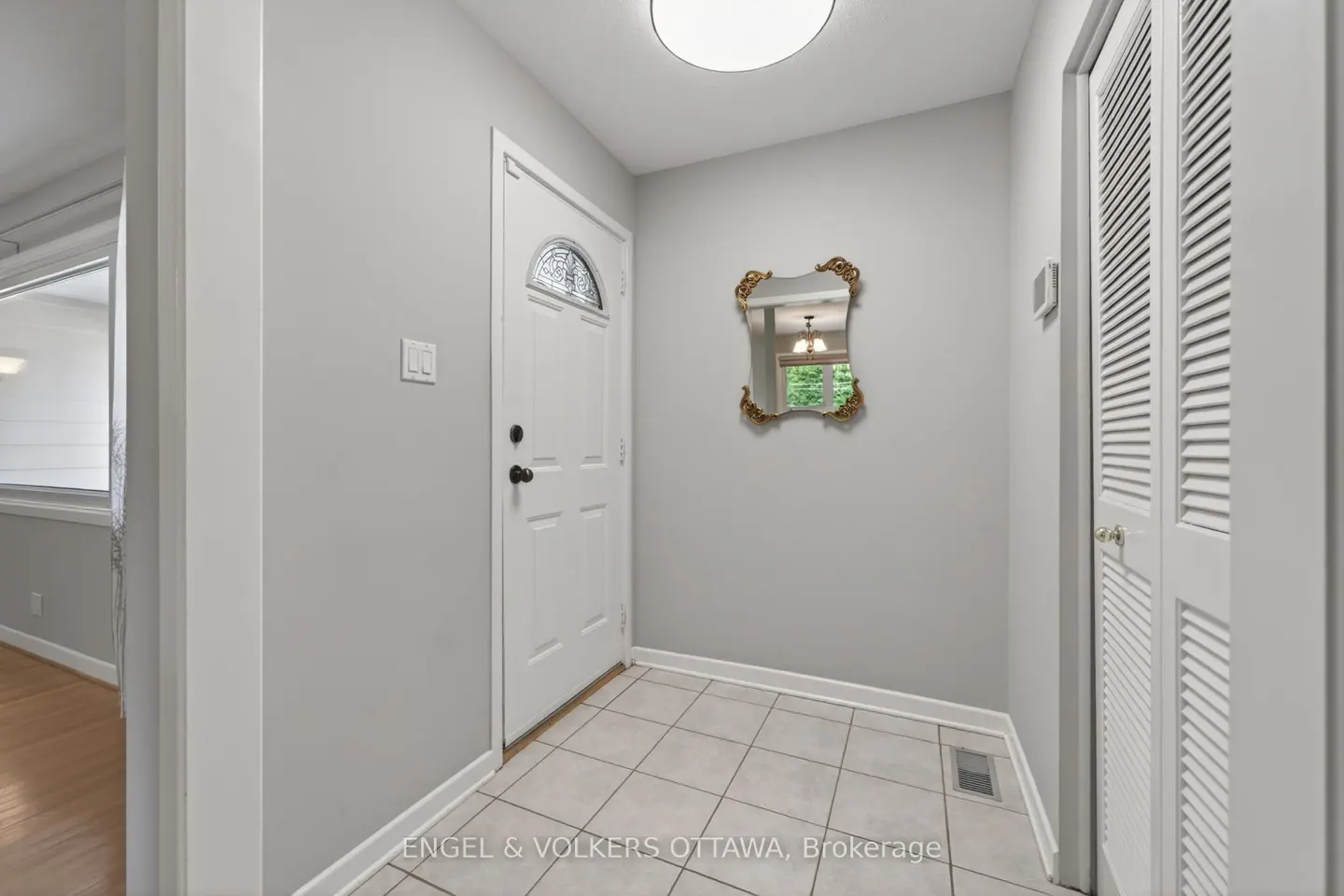 A foyer with gray walls, white trim, and tile floor. A white front door, gold-framed mirror, and white closet door are visible.