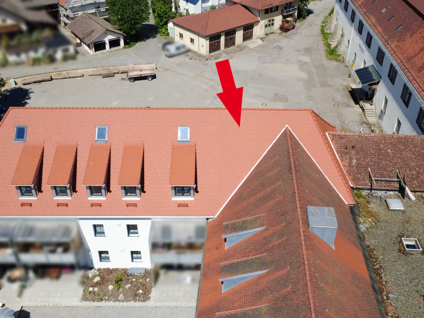 Aerial view of a building with a red tiled roof, dormer windows, and a large red arrow pointing to the roof.