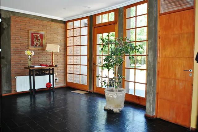 Interior view of a home's entryway with brick wall, wood-framed windows, a potted plant, and dark wood floors.