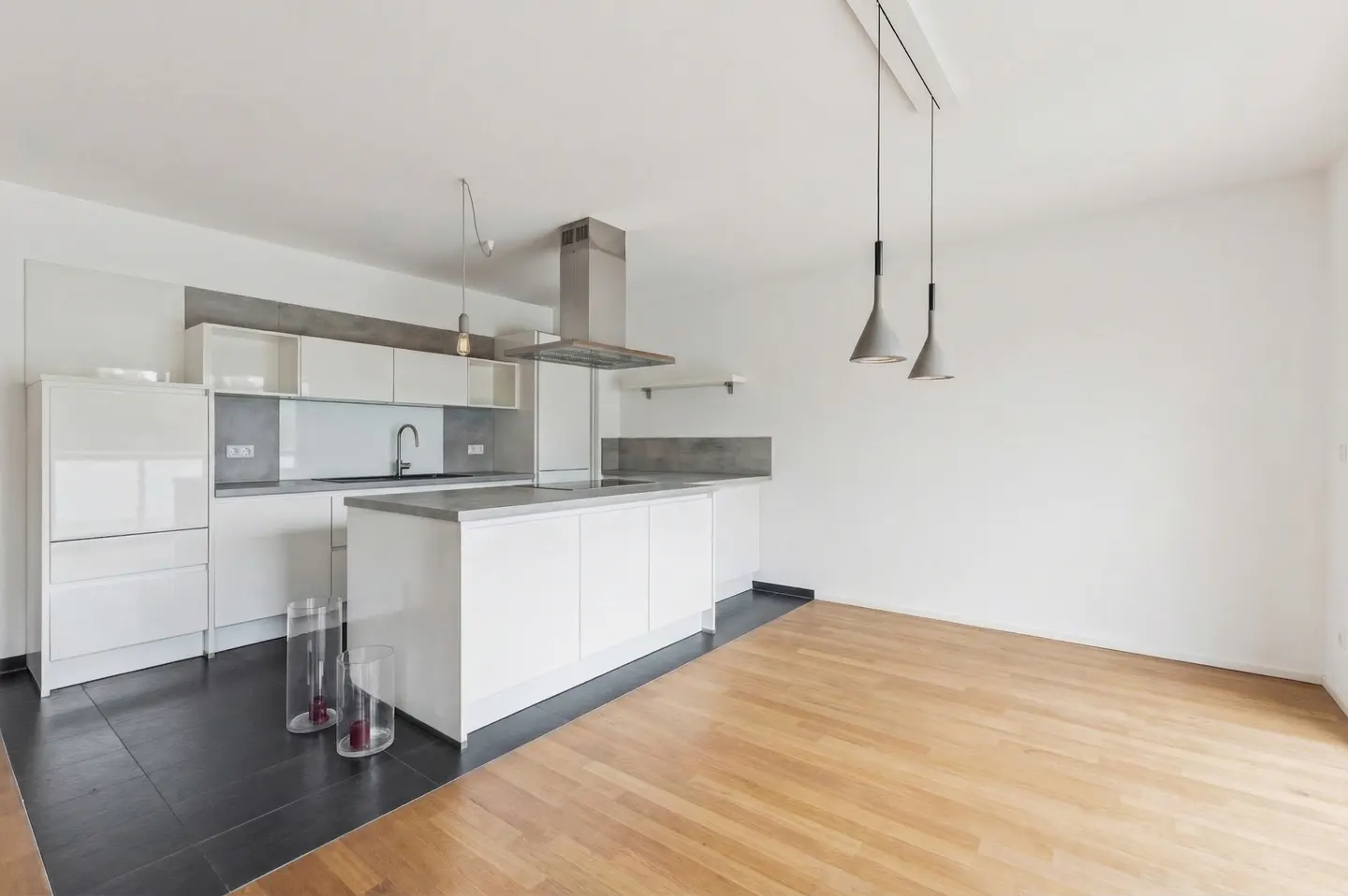 Bright, modern kitchen with white cabinets, gray countertops, and stainless steel appliances. Hardwood floors and pendant lighting add warmth.