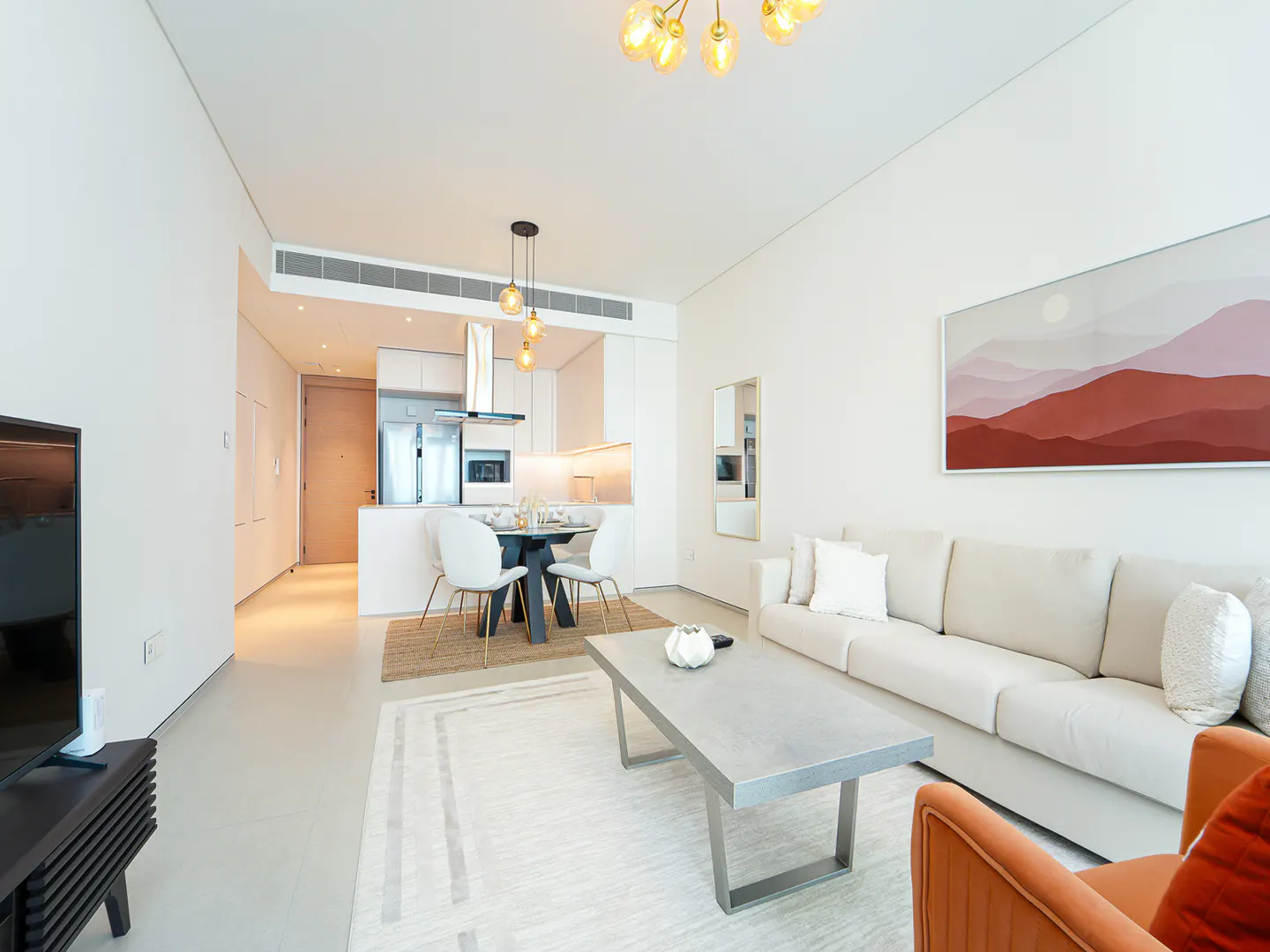 Modern open-plan living room with white sofa, grey coffee table, dining area, and abstract mountain art on a white wall.