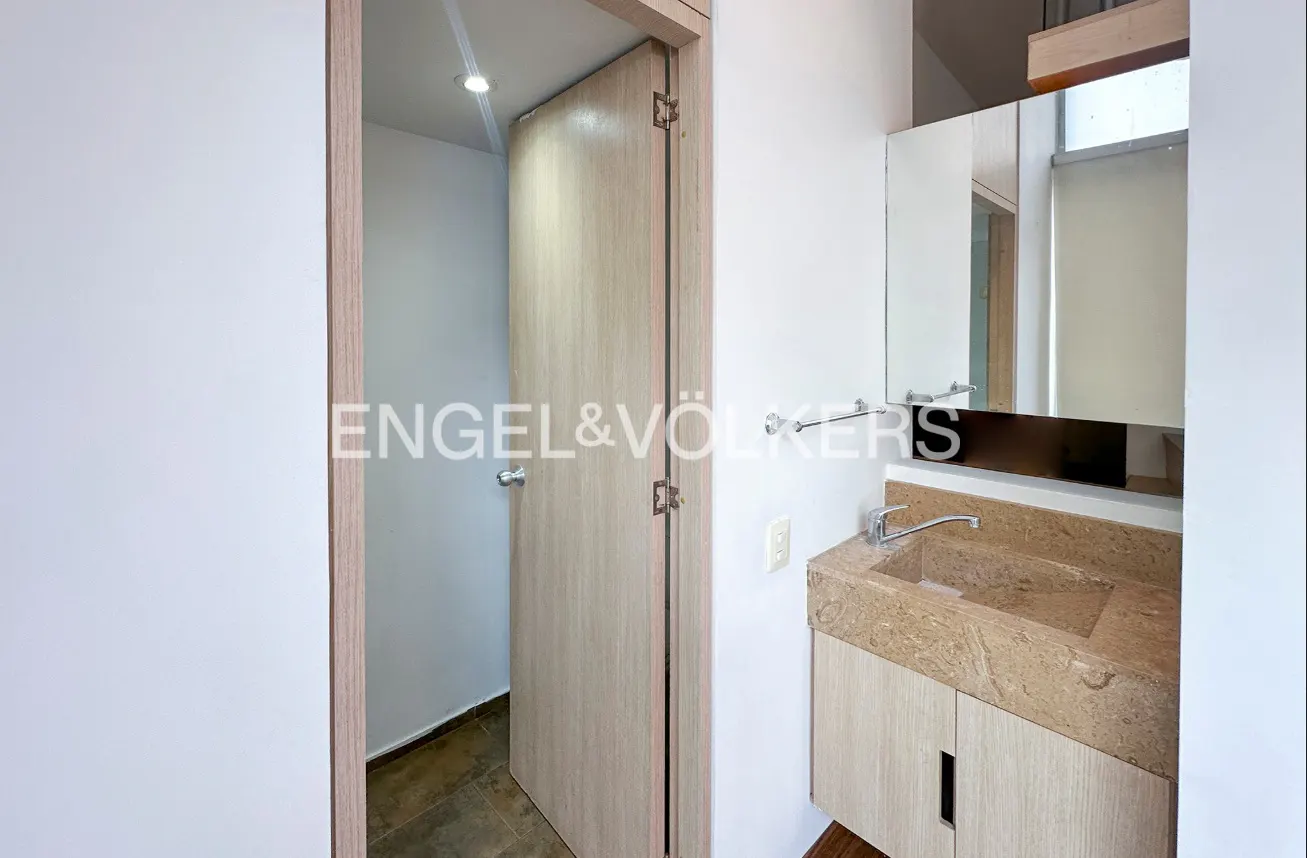 Bathroom with a beige stone sink, a mirror, and a light wood door slightly ajar.