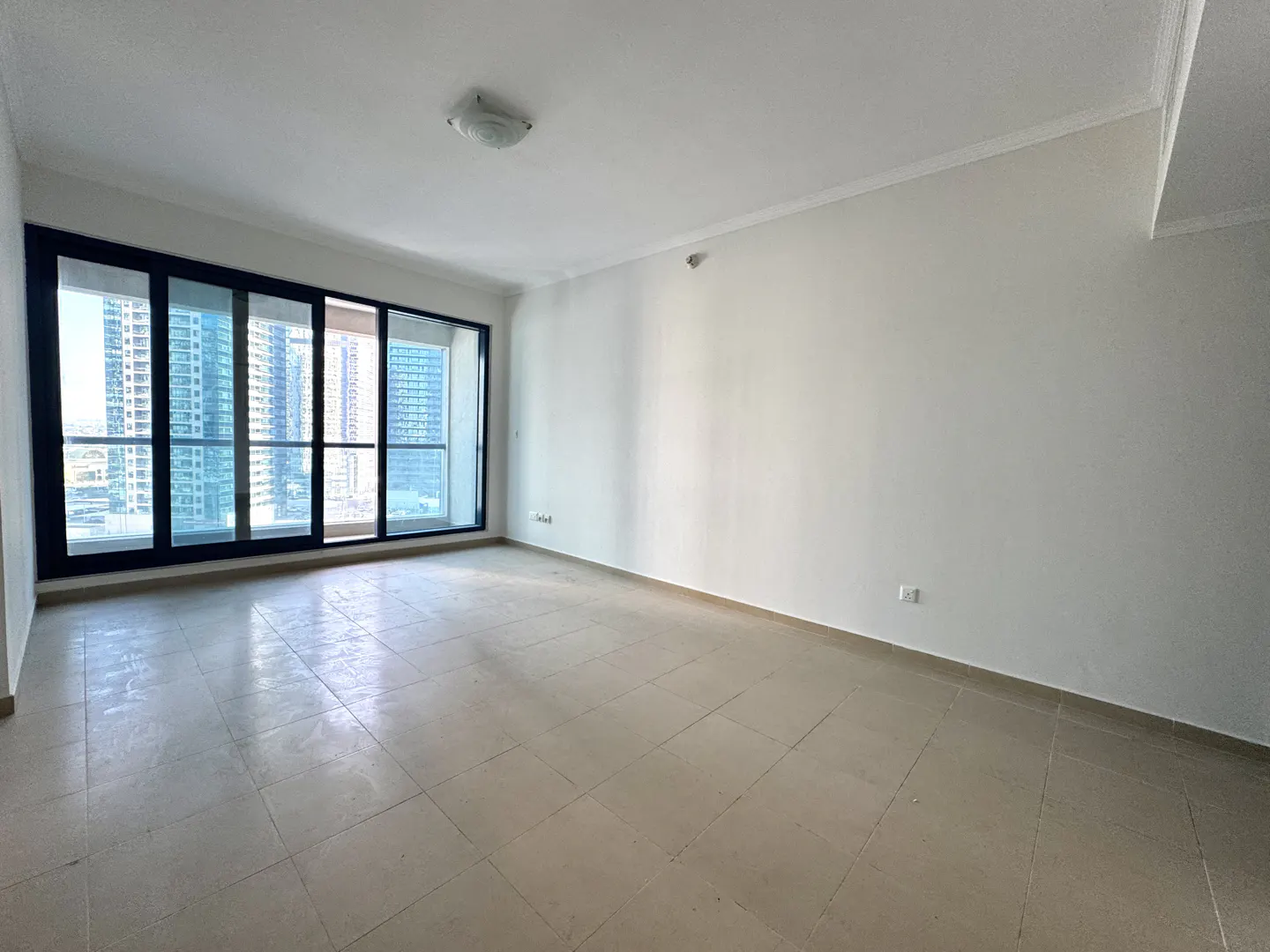 Empty room with beige tile floor, white walls, and a large black-framed window showing a city view.