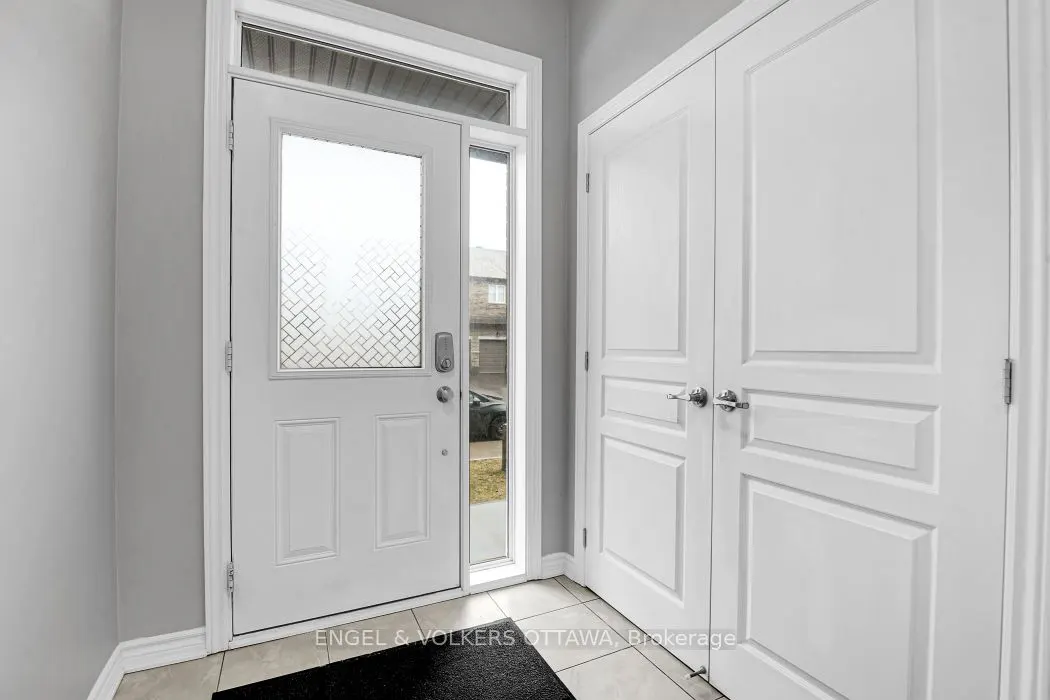 A bright foyer with a white front door with patterned glass, a sidelight, and a double closet with silver handles.