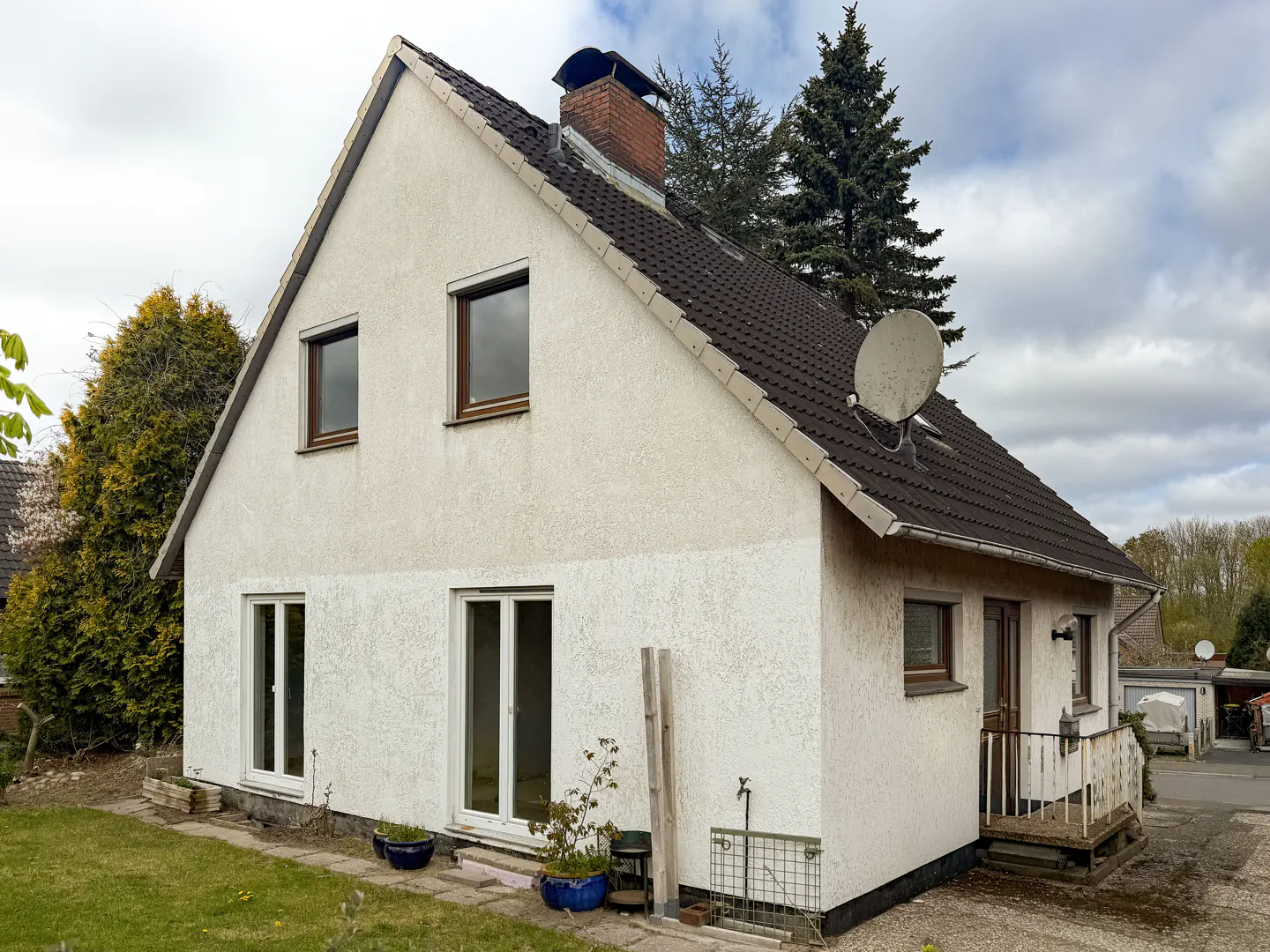 Two-story white stucco house with a dark tiled roof, brick chimney, satellite dish, and a small backyard patio.