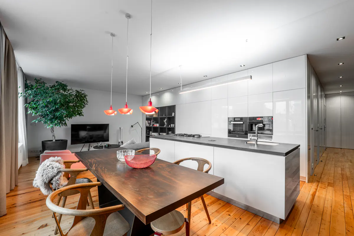 Open-concept living space with a dark wood table, chairs, and red pendant lights. White kitchen island and cabinets in the background.