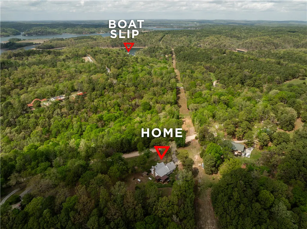Aerial view of a home and boat slip surrounded by green trees and a lake in the background.