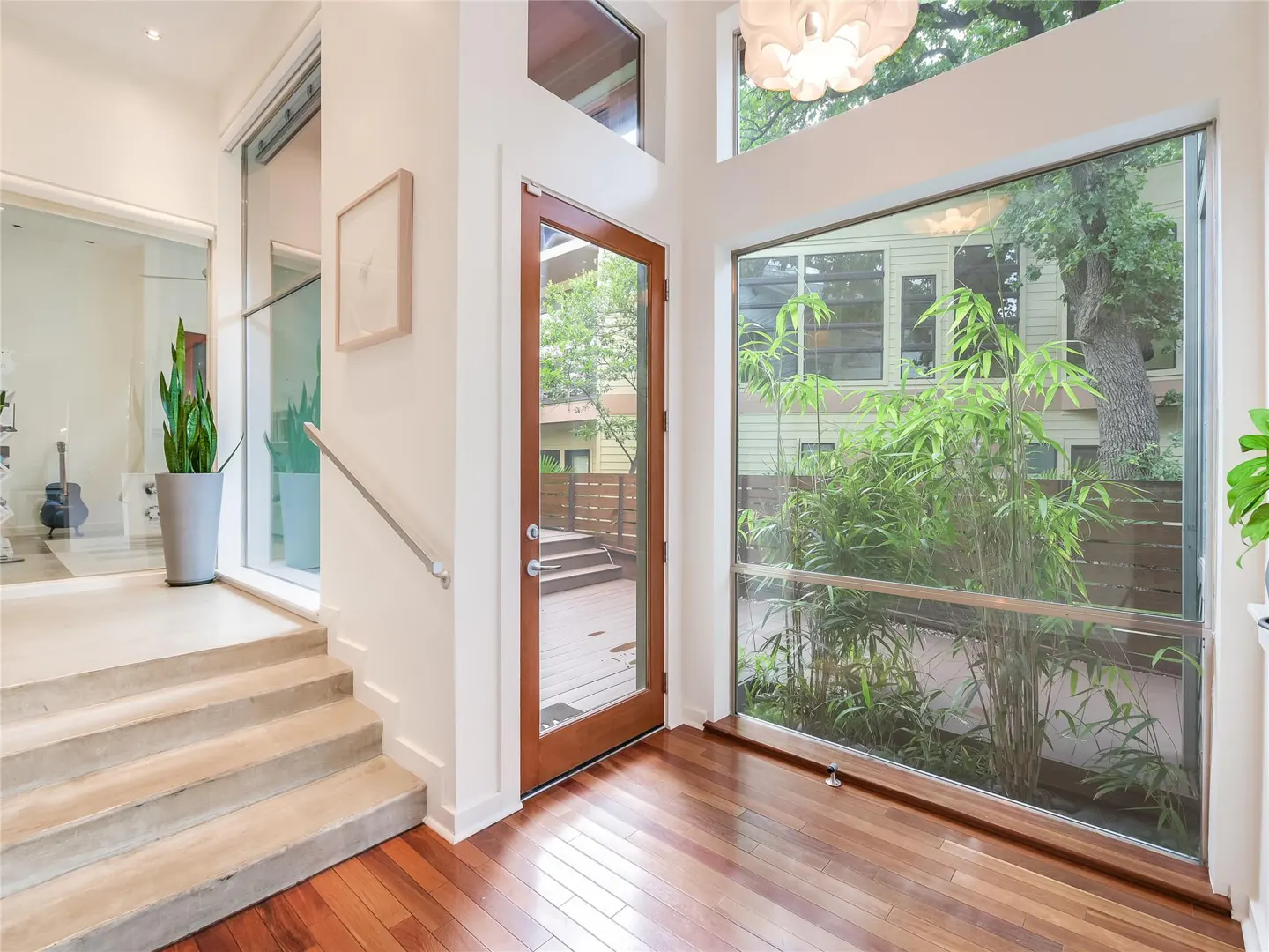 Bright foyer with hardwood floors, white walls, and large windows. A wooden door leads to an outdoor deck. Stairs lead to another room.