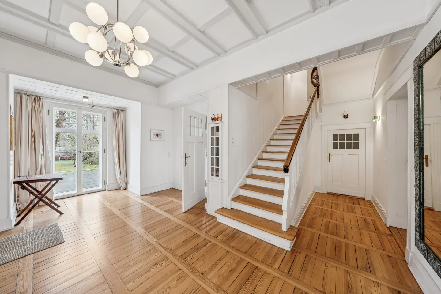 Bright foyer with wood floors, white walls, and a staircase. A modern chandelier hangs from the ceiling. French doors lead to the outside.