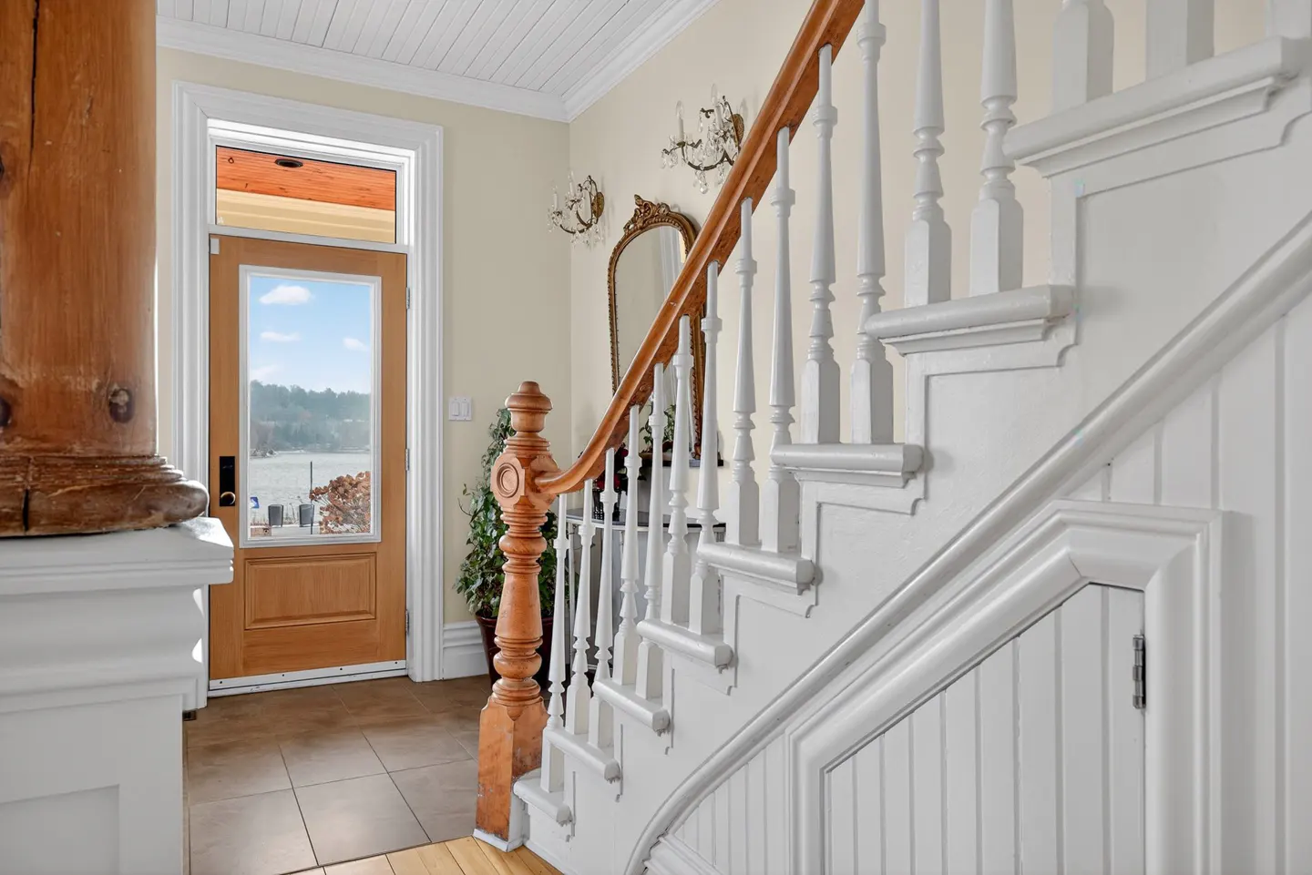 Entryway with white staircase, wooden handrail, and a glass-paneled door revealing a view of a lake.