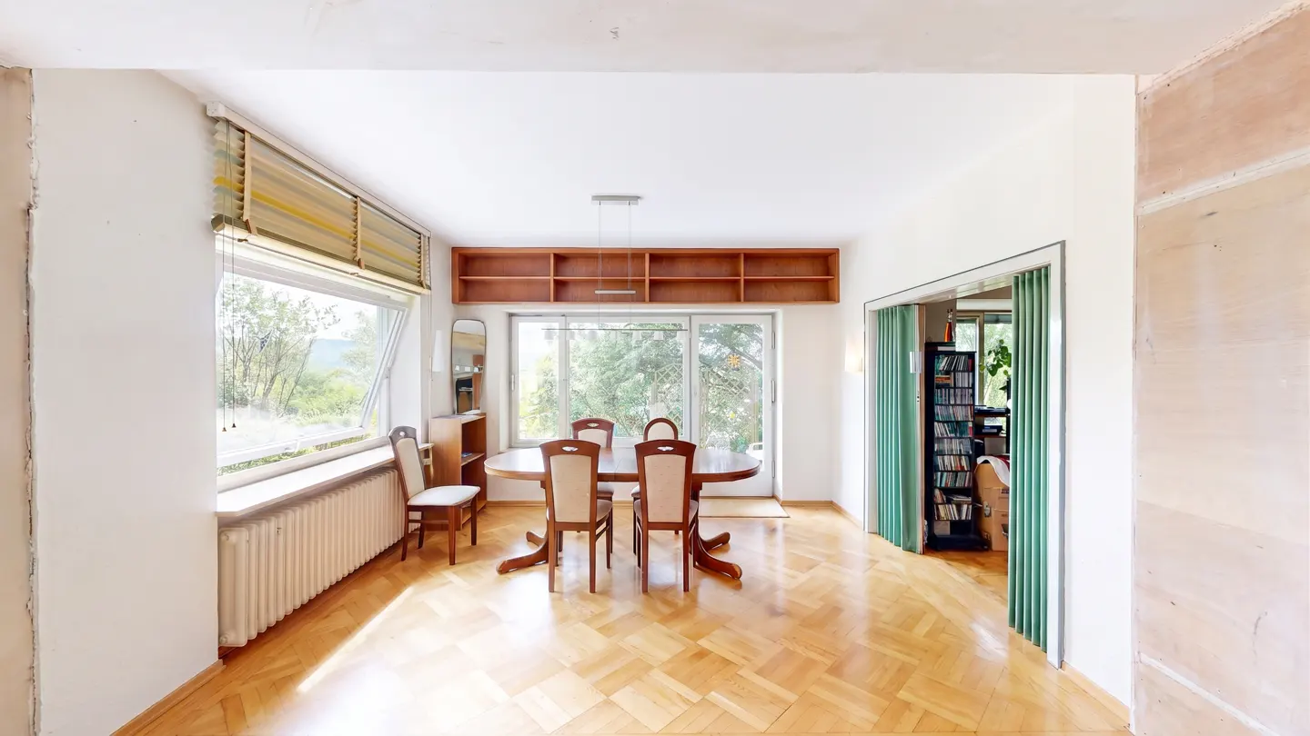 Bright dining room with wood floors, oval table, and four chairs. Large window with view and built-in shelves.