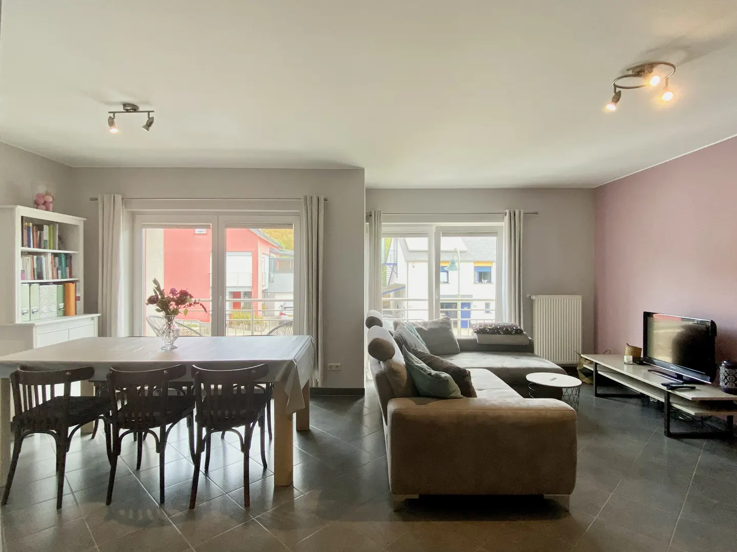 Open-concept living and dining area with gray tile floor, brown sectional sofa, and dining table with black chairs.