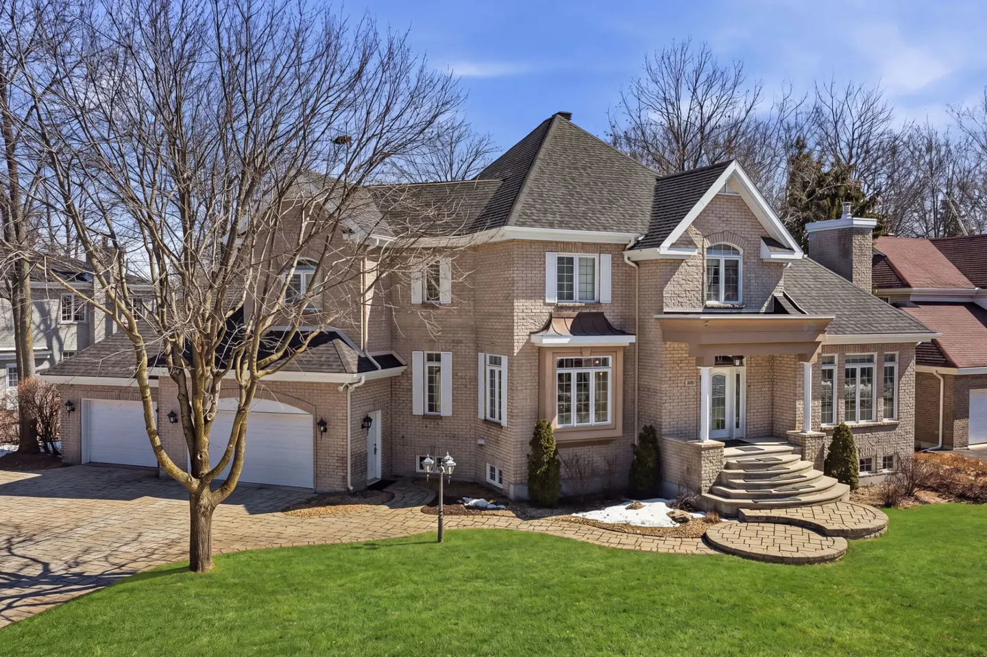 Two-story brick house with a gray roof, white trim, and a stone walkway leading to the front door. Green lawn and bare trees surround the house.