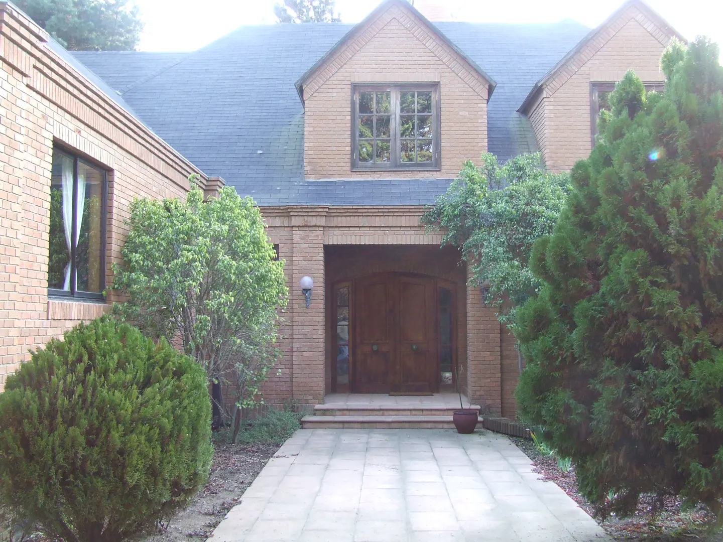 A two-story brick house with a blue roof, a stone walkway, and green bushes.