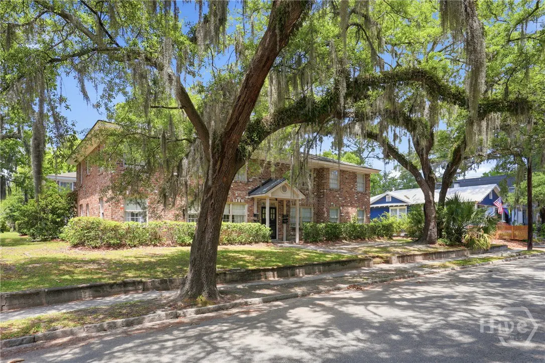 Brick apartment building with a covered entrance, framed by trees with Spanish moss, on a sunny day.