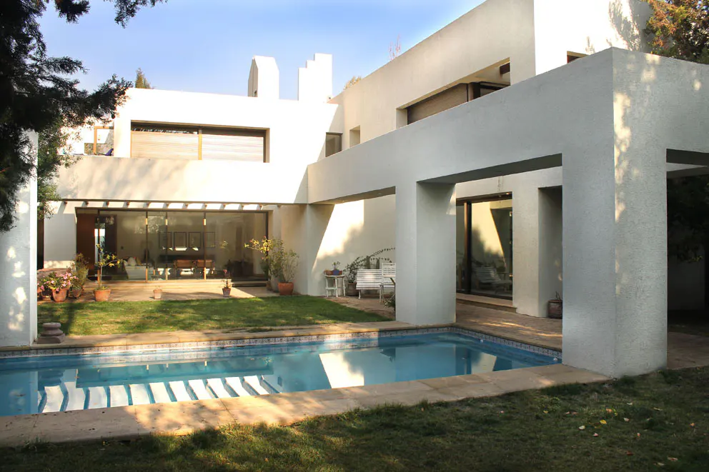Modern white house with a blue tiled pool in the foreground and a green lawn.