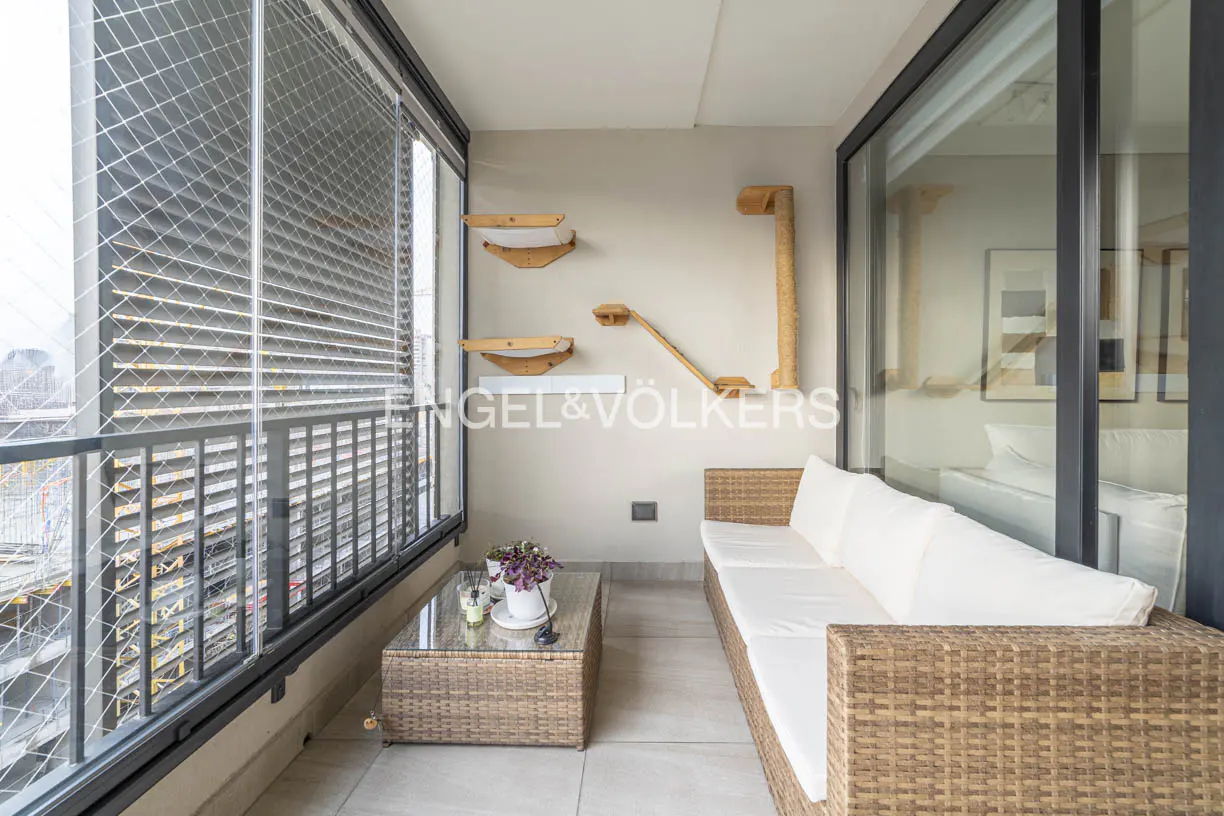 A balcony with a wicker couch, glass table, and cat climbing shelves on the wall.