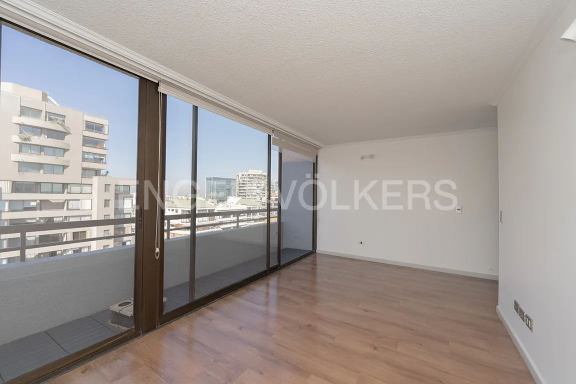 Bright, empty room with light wood floors and white walls. Large sliding glass doors open to a balcony with a city view.