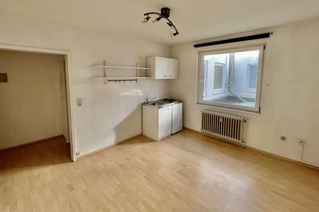 A bright studio apartment with wood floors, a kitchenette, and a window overlooking a courtyard.