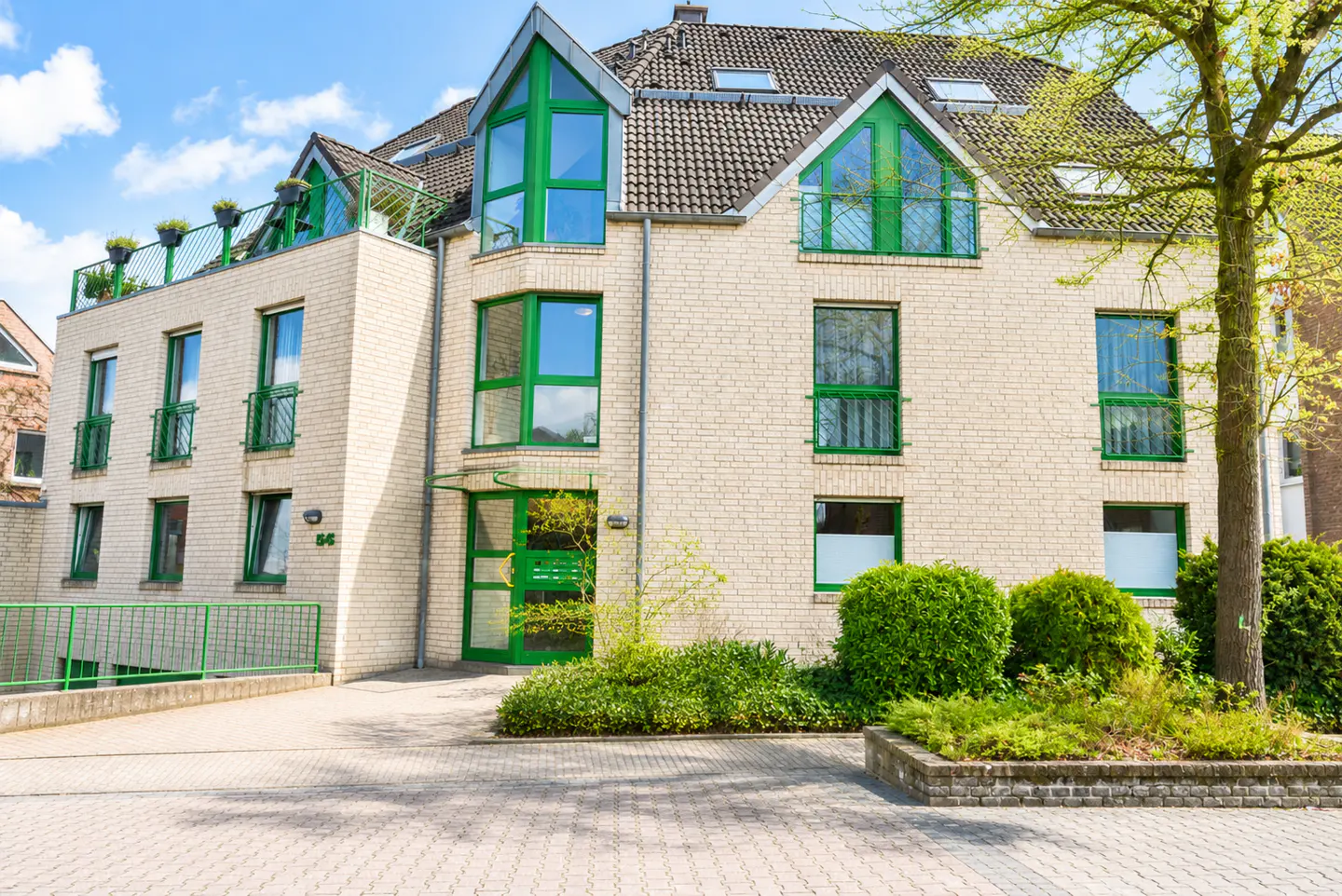 A three-story brick building with green window frames and a rooftop terrace.