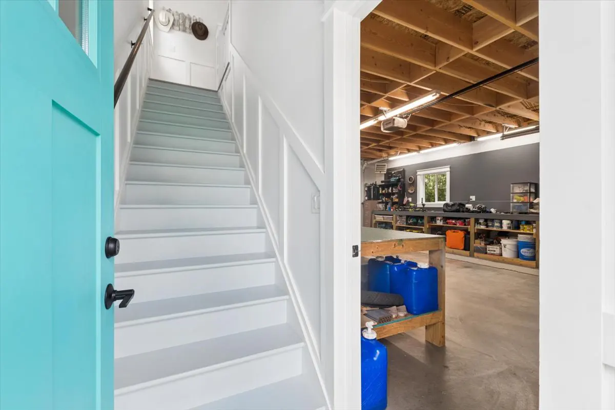 Interior view of a home with a turquoise door, white stairs, and a garage with tools and a workbench.