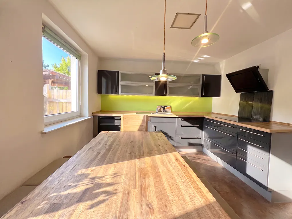 Bright kitchen with gray cabinets, wood countertops, and a large wood table. A window lets in sunlight.